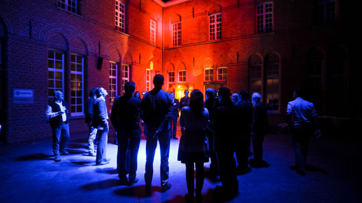 Um grande grupo de pessoas debate no exterior de um edifício bem iluminado em Turnhout, Bélgica, durante um workshop organizado pela Philips