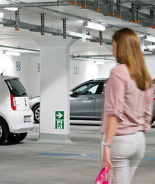 Uma mulher caminha para um carro estacionado num parque de estacionamento ecológico sustentável e brilhante