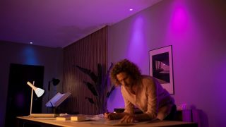 As luzes LED inteligentes Hue Philips criam um ambiente vibrante em tons de roxo e rosa na sala de estar, exibindo iluminação ambiente personalizável para noites de cinema e relaxamento em casas modernas.