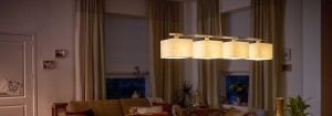 Luminária pendente de LED moderna com diversas cúpulas de tecido ilumina uma sala de estar aconchegante, apresentando soluções de iluminação residencial elegantes e com baixo consumo de energia para um conforto noturno agradável.