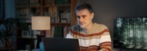Um homem vestindo um suéter listrado está sentado à sua mesa, olhando para o laptop à sua frente.