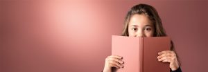 "Jovem espiando por cima de um livro rosa contra um fundo suave iluminado por LED, exibindo uma iluminação quente e uniforme para ambientes de leitura confortáveis."